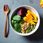 ** A colorful vegetable bowl featuring spinach, roasted red beets, grilled yellow bell peppers, avocado, quinoa, sprinkled with pumpkin seeds and a tahini dressing. Focus on bright, contrasting colors and textures.

**